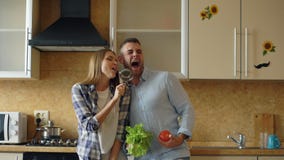 Attractive young joyful couple have fun dancing and singing while cooking in the kitchen at home
