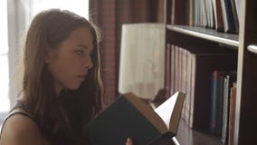 Attractive young woman is choosing a textbook on the library shelves stock video Attractive young woman is choosing a textbook on the library shelves stock video