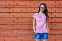 Attractive young woman dressed in a red and white striped t-shirt posing on a background of a red brick wall royalty free stock photography Attractive young woman dressed in a red and white striped t-shirt posing on a background of a red brick wall royalty free stock photography