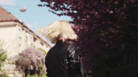Attraktiv blond flicka i läderomslag som charmingly tycker om den körsbärsröda blomningen i staden, vänd till kameran och leenden arkivfilmer Attraktiv blond flicka i läderomslag som charmingly tycker om den körsbärsröda blomningen i staden, vänd till kameran och leenden arkivfilmer