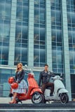 Attraktiva romantiska par, en stilig man och sexig kvinnlig som står med två retro italienska sparkcyklar mot a arkivfoto Attraktiva romantiska par, en stilig man och sexig kvinnlig som står med två retro italienska sparkcyklar mot a arkivfoto