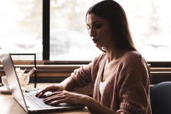 Attraktive junge Frau sitzt an einem Tisch in einem Caf? mit einem Tasse Kaffee und genie?t einen Laptop lizenzfreie stockfotos Attraktive junge Frau sitzt an einem Tisch in einem Caf? mit einem Tasse Kaffee und genie?t einen Laptop lizenzfreie stockfotos