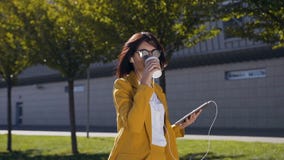 Attraktive junge Geschäftsfrau in der Sonnenbrille trinkt Kaffee während sie eine Mitteilung auf Tablet-Computer sendend draußen stock video Attraktive junge Geschäftsfrau in der Sonnenbrille trinkt Kaffee während sie eine Mitteilung auf Tablet-Computer sendend draußen stock video