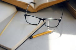 Auf dem Tisch gibt es Enzyklopädien, ein Notizbuch, einen Bleistift und elegante Gläser lizenzfreies stockfoto Auf dem Tisch gibt es Enzyklopädien, ein Notizbuch, einen Bleistift und elegante Gläser lizenzfreies stockfoto