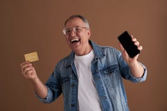 Aufgeregtes erwachsenes Lachen beim Zeigen seiner Smartphone- und Goldkarte stockfotografie Aufgeregtes erwachsenes Lachen beim Zeigen seiner Smartphone- und Goldkarte stockfotografie