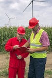 Aufsichtskraft im roten Hardhat sprechend mit Arbeitskraft am Windpark lizenzfreies stockbild Aufsichtskraft im roten Hardhat sprechend mit Arbeitskraft am Windpark lizenzfreies stockbild