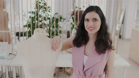 Ausdrucksvoller und reizend Modedesigner, der die Kamera bei der Stellung in ihrem modernen nähenden Büro oder in Atelier untersu stock footage Ausdrucksvoller und reizend Modedesigner, der die Kamera bei der Stellung in ihrem modernen nähenden Büro oder in Atelier untersu stock footage