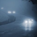 Auto's in de mist Slecht de winterweer en gevaarlijk automobiel verkeer op de weg Lichte voertuigen in mist stock foto Auto's in de mist Slecht de winterweer en gevaarlijk automobiel verkeer op de weg Lichte voertuigen in mist stock foto