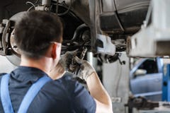 Automechaniker, der Autorad und Reparatursuspendierungsdetail kontrolliert Angehobenes Automobil an der Reparaturtankstelle wiede lizenzfreies stockfoto Automechaniker, der Autorad und Reparatursuspendierungsdetail kontrolliert Angehobenes Automobil an der Reparaturtankstelle wiede lizenzfreies stockfoto
