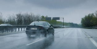 Automobile nera che attraversa through la pioggia persistente sulla strada principale immagine stock libera da diritti Automobile nera che attraversa through la pioggia persistente sulla strada principale immagine stock libera da diritti