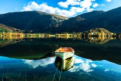 Autumn Landscape avec un bateau solitaire, des montagnes, des arbres colorés et un ciel bleu reflétés dans le lac photos stock Autumn Landscape avec un bateau solitaire, des montagnes, des arbres colorés et un ciel bleu reflétés dans le lac photos stock