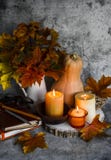 Autumn still life. Lit candles, bouquet of maple leaves, books, pumpkin on a gray background
