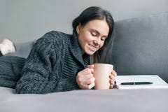 Autumn winter portrait of young girl in warm knitted sweater at home on sofa with notebook and cup of hot drink royalty free stock photo Autumn winter portrait of young girl in warm knitted sweater at home on sofa with notebook and cup of hot drink royalty free stock photo