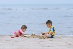 Aziaat weinig jongen en zijn babyzuster die samen op het zandige strand spelen Stock Afbeelding Aziaat weinig jongen en zijn babyzuster die samen op het zandige strand spelen Stock Afbeelding