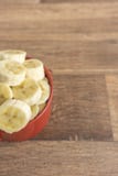 Bacia vermelha com fatias da banana no fundo de madeira imagem de stock royalty free Bacia vermelha com fatias da banana no fundo de madeira imagem de stock royalty free