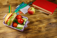Back to school concept. School supplies, books, apple and lunch box with burgers and fresh vegetables on wooden table
