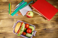 Back to school concept. School supplies, books, apple and lunch box with burgers and fresh vegetables on wooden table. Top view