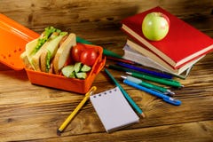 Back to school concept. School supplies, books, apple and lunch box with sandwiches and fresh vegetables on wooden desk