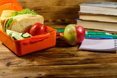 Back to school concept. School supplies, books, apple and lunch box with sandwiches and fresh vegetables on wooden desk
