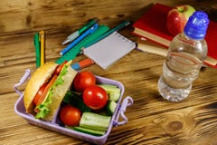 Back to school concept. School supplies, books, bottle of water, apple and lunch box with burgers and fresh vegetables