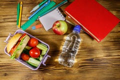 Back to school concept. School supplies, books, bottle of water, apple and lunch box with burgers and fresh vegetables