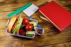 Back to school concept. School supplies, books and lunch box with burgers and fresh vegetables on wooden table