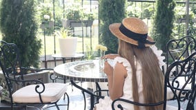 Backshot de la pequeña muchacha bonita en el sombrero de paja que se sienta en un café de la calle que bebe el chocolate caliente metrajes Backshot de la pequeña muchacha bonita en el sombrero de paja que se sienta en un café de la calle que bebe el chocolate caliente metrajes