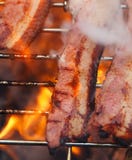 Baconkött på bbq-grillfestgaller med brand Royaltyfria Bilder Baconkött på bbq-grillfestgaller med brand Royaltyfria Bilder