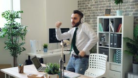 Baile hermoso del hombre joven que escucha la música en auriculares en oficina moderna almacen de metraje de vídeo Baile hermoso del hombre joven que escucha la música en auriculares en oficina moderna almacen de metraje de vídeo