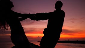 Baile joven romántico de la silueta de los pares que lleva a cabo las manos y que hace girar alrededor en una puesta del sol asom metrajes Baile joven romántico de la silueta de los pares que lleva a cabo las manos y que hace girar alrededor en una puesta del sol asom metrajes