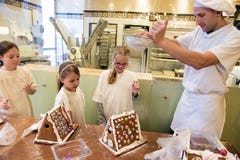 Gingerbread house baking in the run up to Christmas. Baker shows children how to sprinkle powdered sugar over gingerbread house