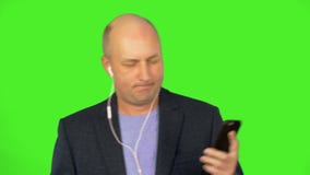Bald adult caucasian man listen to music at smart phone via earphones and dance. Dancing man in blue suit listen music