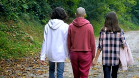 Bald woman, mother and her teenage children walk together in a park or forest stock video footage Bald woman, mother and her teenage children walk together in a park or forest stock video footage