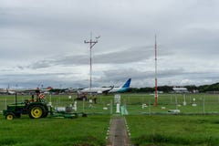 BALI/INDONESIA- 21 DICEMBRE 2019: alcuni pulitori dell'aeroporto hanno tagliato l'erba intorno alla pista facendo uso di una falc immagine stock BALI/INDONESIA- 21 DICEMBRE 2019: alcuni pulitori dell'aeroporto hanno tagliato l'erba intorno alla pista facendo uso di una falc immagine stock