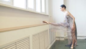Ballerina im Stadiumskleid, das Bein in der vertikalen Spalte nahe Fenster in der Klasse ausdehnt stock video footage Ballerina im Stadiumskleid, das Bein in der vertikalen Spalte nahe Fenster in der Klasse ausdehnt stock video footage