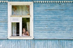 Bambina annoiata triste che guarda fuori la finestra della casa di campagna che pende il suo fronte sulla sua mano Immagini Stock Bambina annoiata triste che guarda fuori la finestra della casa di campagna che pende il suo fronte sulla sua mano Immagini Stock