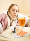 Bambina con influenza che si trova a letto e che esamina tazza di tè immagine stock Bambina con influenza che si trova a letto e che esamina tazza di tè immagine stock