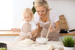 Bambina e la sua mamma bionda in grembiuli beige che giocano e che ridono mentre impastando la pasta nella cucina Homemad Fotografia Stock Libera da Diritti Bambina e la sua mamma bionda in grembiuli beige che giocano e che ridono mentre impastando la pasta nella cucina Homemad Fotografia Stock Libera da Diritti