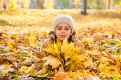Bambina sveglia che si trova sulle foglie cadute e che tiene il mazzo delle foglie di acero gialle in mani fotografia stock Bambina sveglia che si trova sulle foglie cadute e che tiene il mazzo delle foglie di acero gialle in mani fotografia stock
