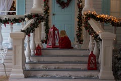 Bambina in vestito rosso che si siede sulla veranda della casa decorata, luci di Natale, ` s EVE del nuovo anno dopo saranno le l fotografia stock Bambina in vestito rosso che si siede sulla veranda della casa decorata, luci di Natale, ` s EVE del nuovo anno dopo saranno le l fotografia stock
