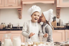 Bambini in cucina La sorella sta dicendo al fratello un segreto mentre cucinava immagini stock Bambini in cucina La sorella sta dicendo al fratello un segreto mentre cucinava immagini stock
