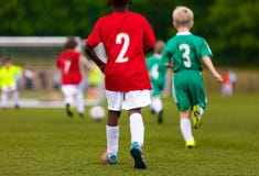 Bambini multirazziali che danno dei calci al calcio sul campo sportivo fotografia stock Bambini multirazziali che danno dei calci al calcio sul campo sportivo fotografia stock