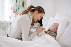 Bambino malato sveglio, neonato, restante a letto, mamma le che dà medici Fotografie Stock Bambino malato sveglio, neonato, restante a letto, mamma le che dà medici Fotografie Stock