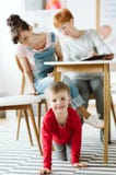 Bambino maleducato che si siede sotto la tavola durante la terapia per ADHD con la suoi madre e terapista professionista fotografia stock Bambino maleducato che si siede sotto la tavola durante la terapia per ADHD con la suoi madre e terapista professionista fotografia stock