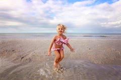 Bambino sveglio che spruzza e che gioca nell'acqua sulla spiaggia dall'oceano fotografia stock Bambino sveglio che spruzza e che gioca nell'acqua sulla spiaggia dall'oceano fotografia stock