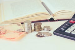 Banconota dei soldi, monete in mucchi, un calcolatore davanti ad un libro aperto Il concetto di istruzione costosa e di borsa di fotografia stock Banconota dei soldi, monete in mucchi, un calcolatore davanti ad un libro aperto Il concetto di istruzione costosa e di borsa di fotografia stock