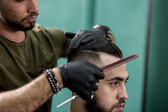 Barber in black gloves combs hair of stylish man at a barbershop royalty free stock image Barber in black gloves combs hair of stylish man at a barbershop royalty free stock image