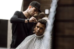 The barber dressed in black clothes makes a razor cut hair back and sides for a stylish man sitting in the armchair in a stock photography The barber dressed in black clothes makes a razor cut hair back and sides for a stylish man sitting in the armchair in a stock photography