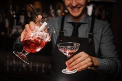 Barista sorridente che versa un cocktail alcolico fresco nel vetro di cocktail immagini stock Barista sorridente che versa un cocktail alcolico fresco nel vetro di cocktail immagini stock
