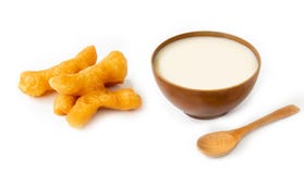 Bastoni fritti nel grasso bollente della pasta e latte di soia isolato su fondo bianco, cucchiaio di legno immagine stock libera da diritti Bastoni fritti nel grasso bollente della pasta e latte di soia isolato su fondo bianco, cucchiaio di legno immagine stock libera da diritti